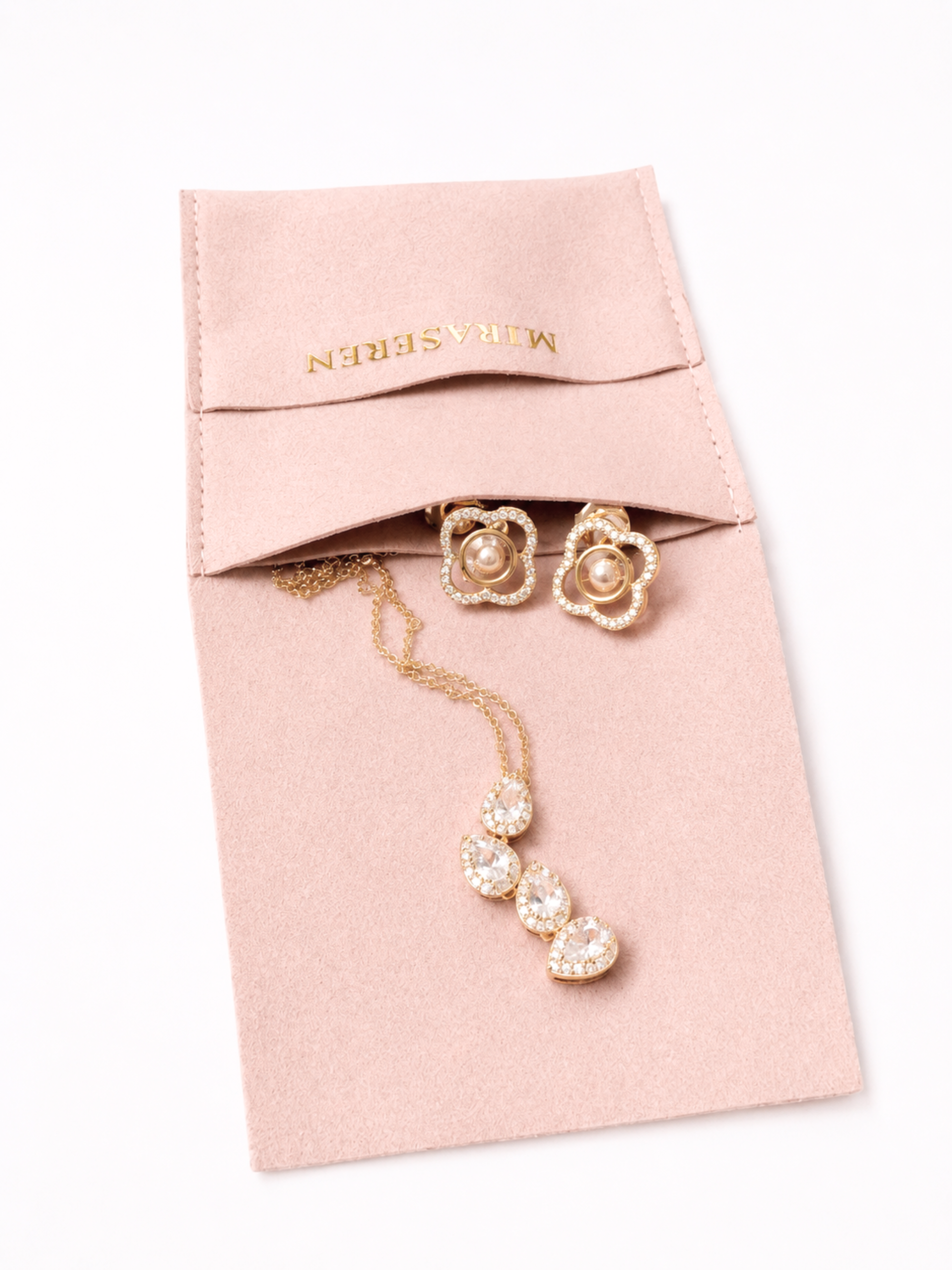 A gold jewelry set with pearl and crystal details, including a flower-shaped pair of earrings and a matching pendant necklace, displayed on a pink velvet jewelry pouch with the brand name MAASERIN visible on the inside flap.