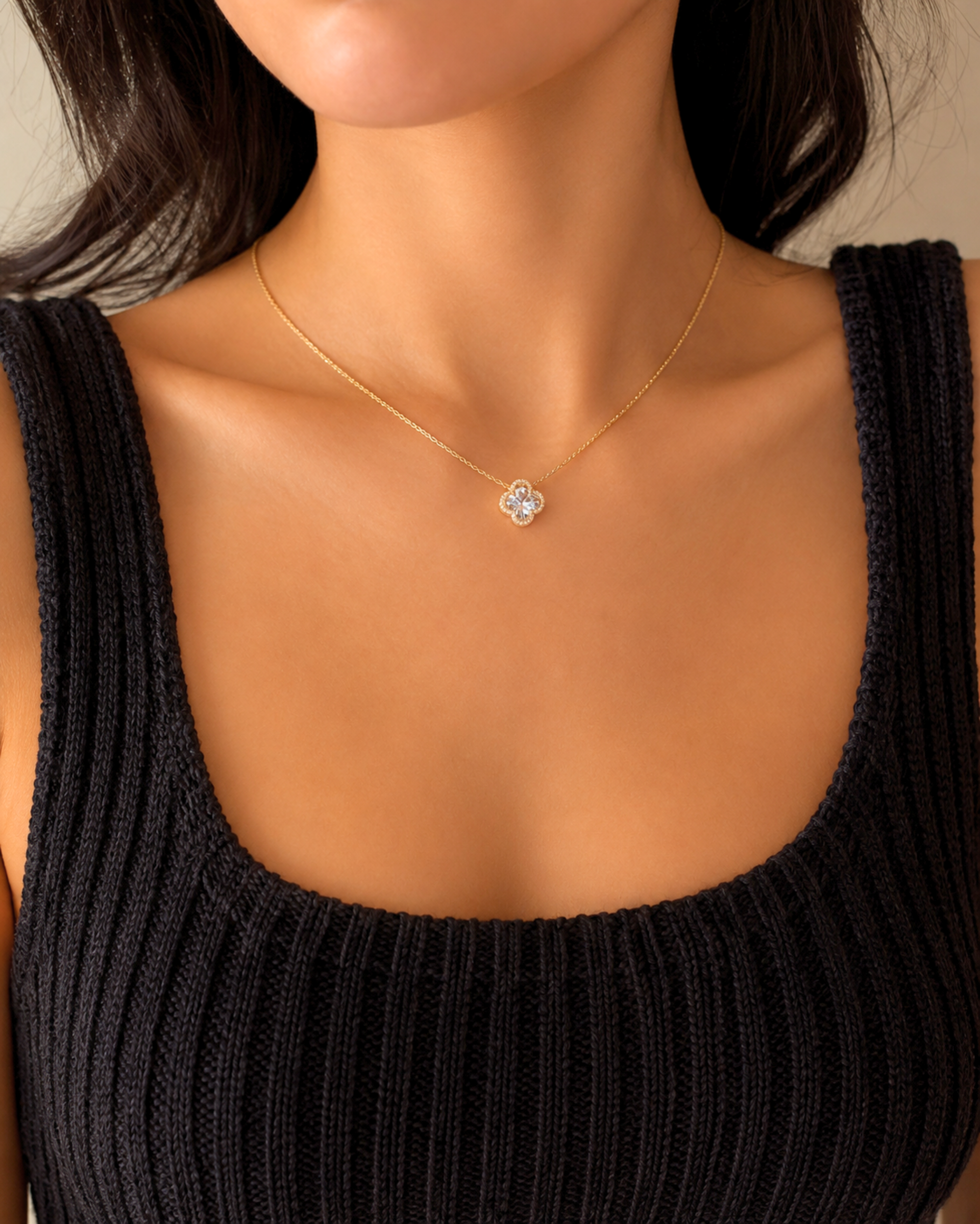 A close-up of a model wearing a delicate gold chain necklace with a small heart-shaped pendant set with clear stones, paired with a black ribbed knit top.