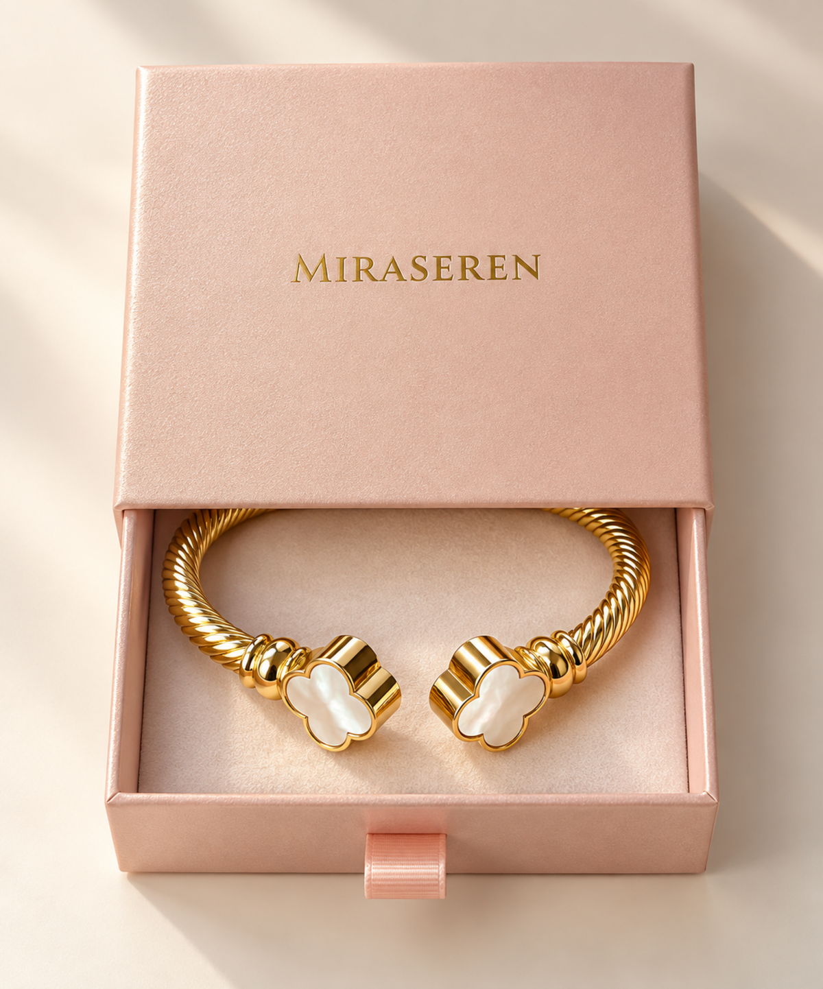 A Miraseren gold-plated twist bracelet with two clover-shaped white mother-of-pearl accents, presented inside a pink gift box.