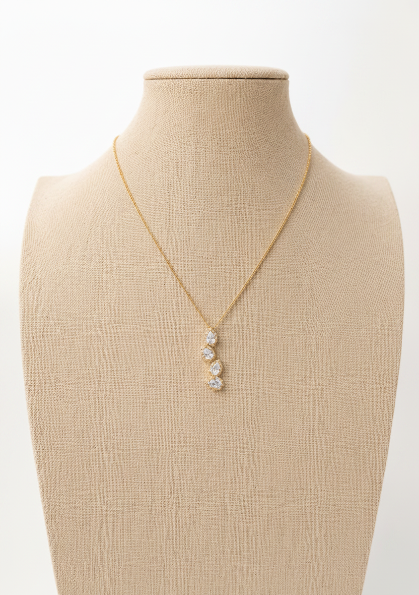 A gold chain necklace with a three-stone drop pendant set with clear stones, displayed on a beige fabric jewelry bust against a white background.