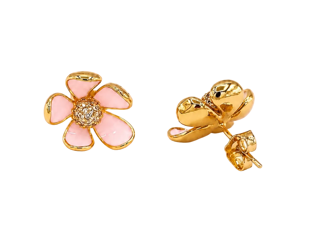 A pair of gold flower stud earrings with light pink enamel petals and a small clear crystal center, shown on a plain light pink background.