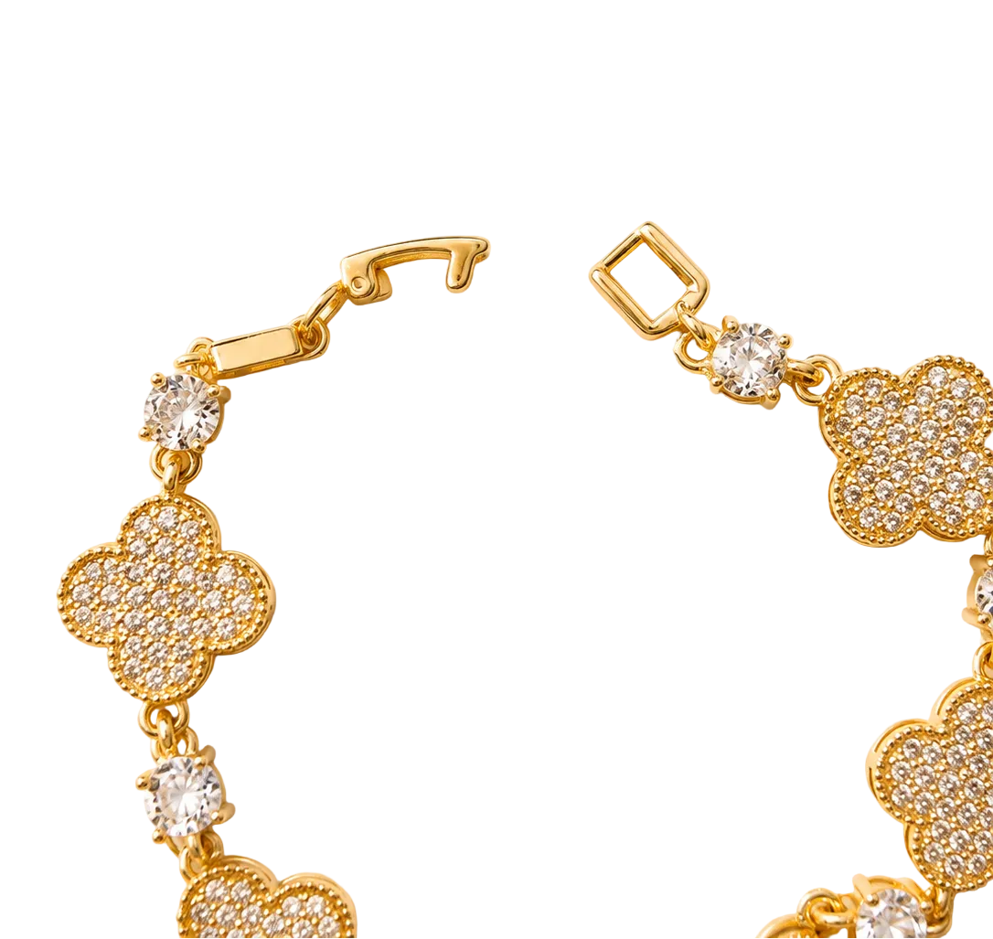 Gold-tone bracelet with pavé four-leaf clover motifs and clear round accent stones, photographed on a warm cream background.