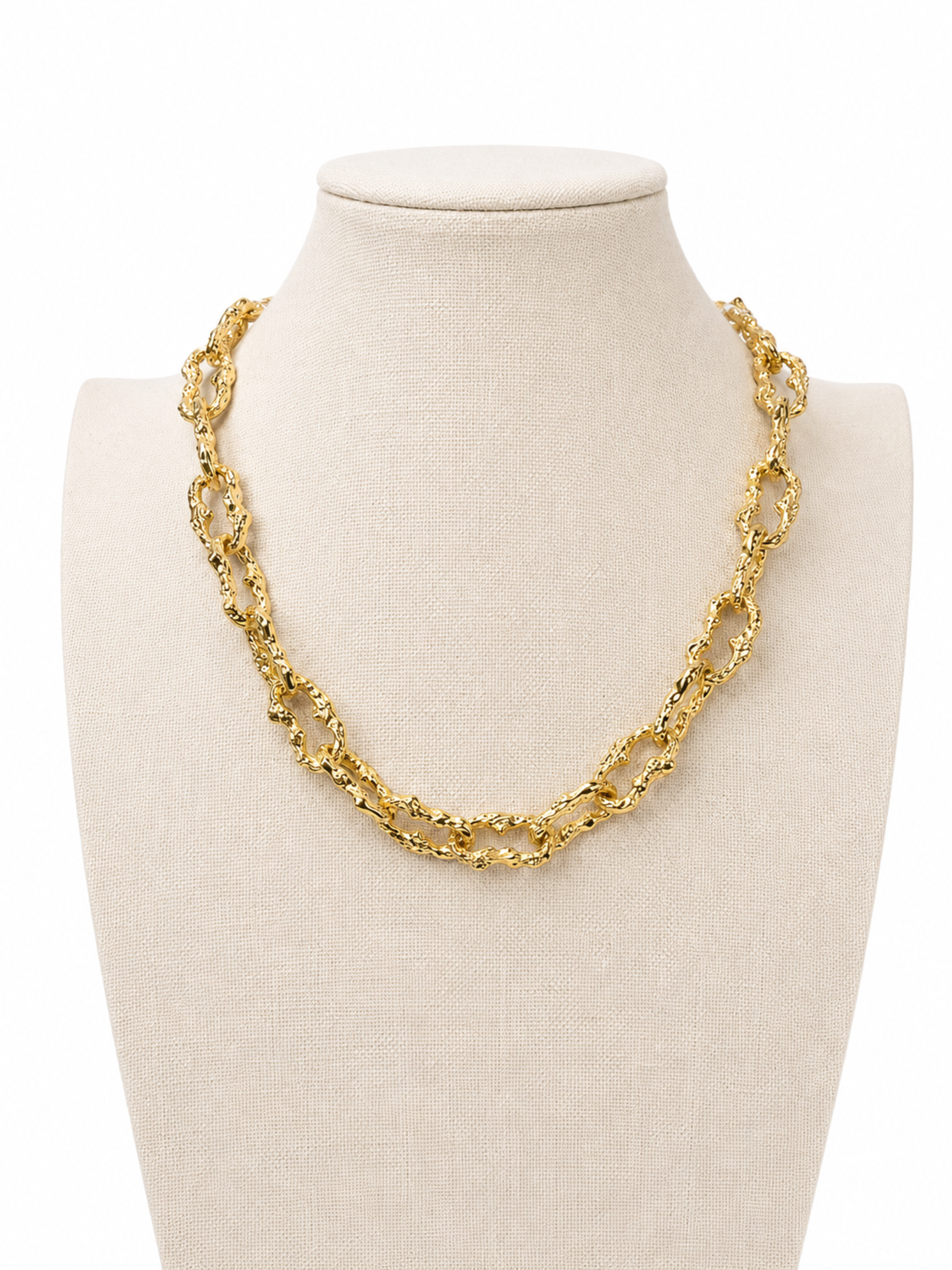 A chunky gold chain link necklace displayed on a cream fabric jewelry bust against a white background.