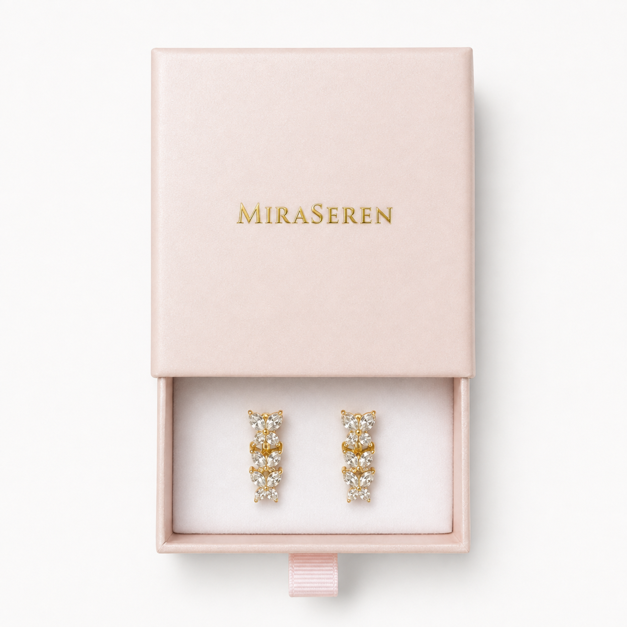 MiraSeren gold hoop earrings with clear crystals, presented in a light pink jewelry box with the brand name in gold lettering.