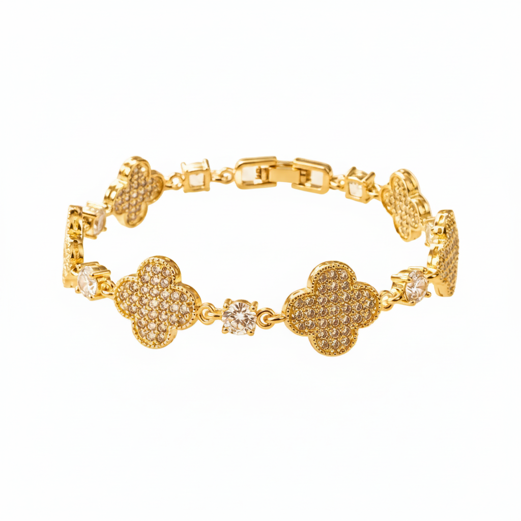 A gold-plated bracelet featuring four clover-shaped links paved with small clear stones, accented by three loose clear cubic zirconia stones, shown on a warm beige background.