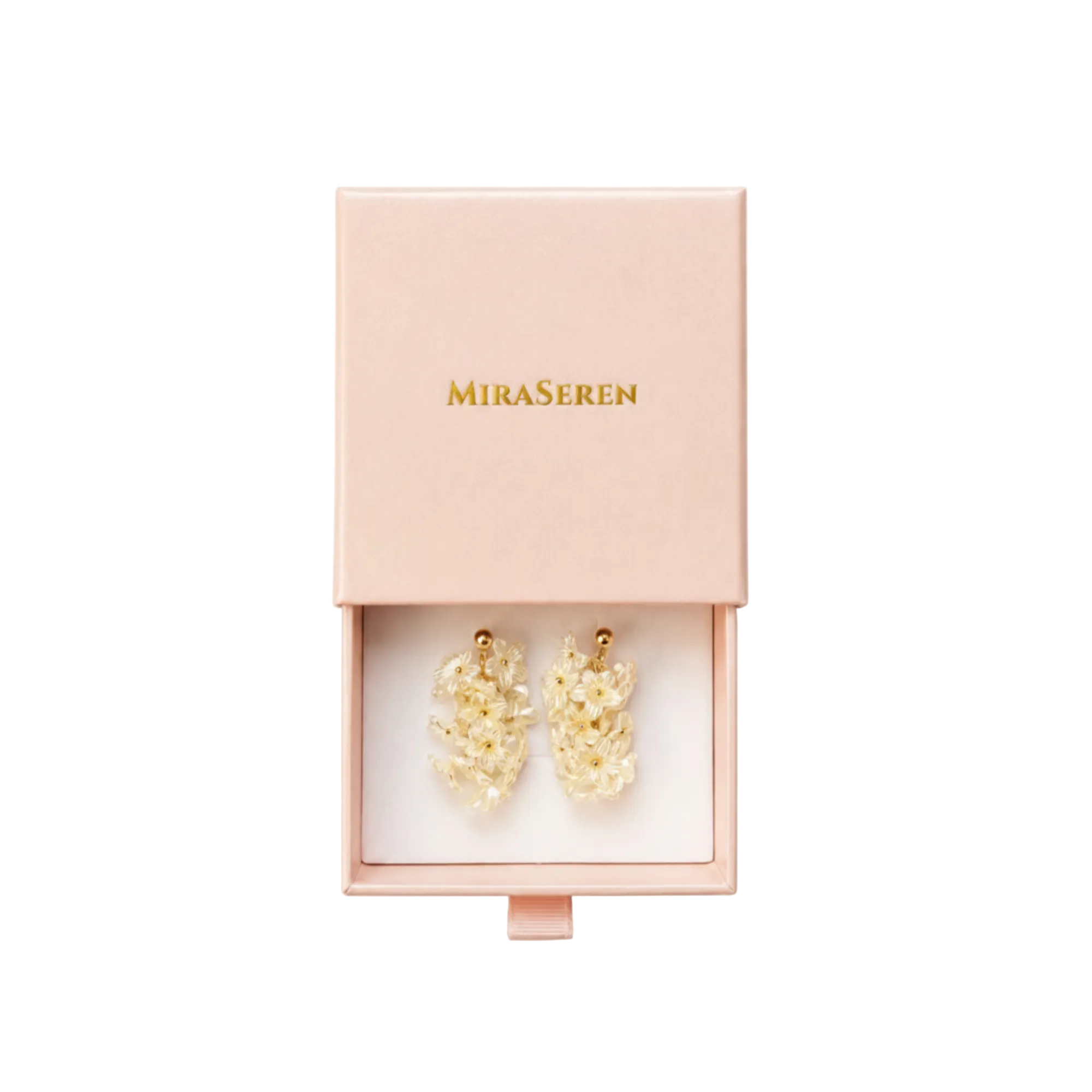 A pair of gold-toned drop earrings with delicate white floral clusters, presented in an open light pink Miraseren jewelry box on a white background.