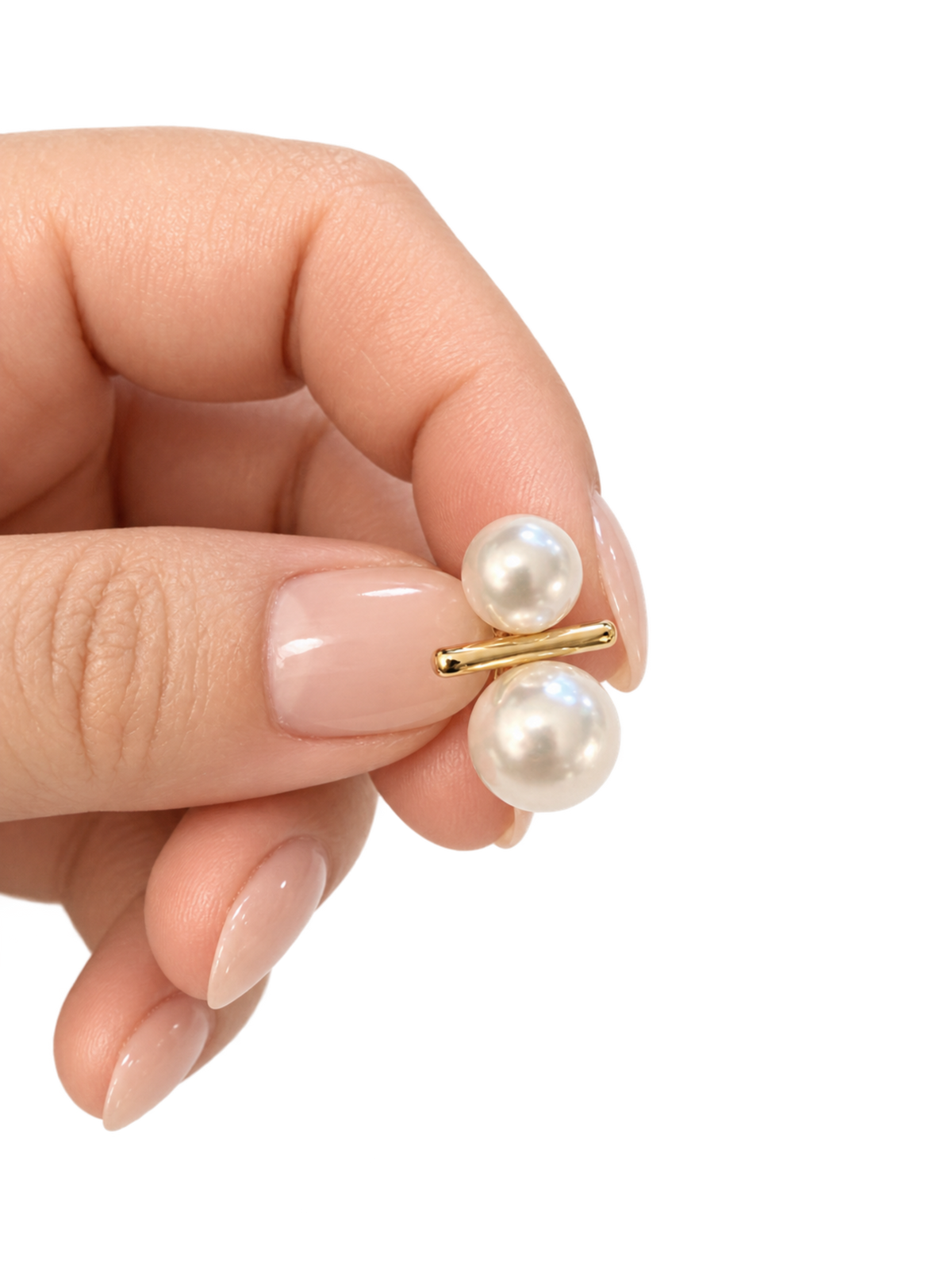 A close-up of a hand with manicured nails holding a small gold-tone stud earring with two white pearl-like beads on a plain white background.