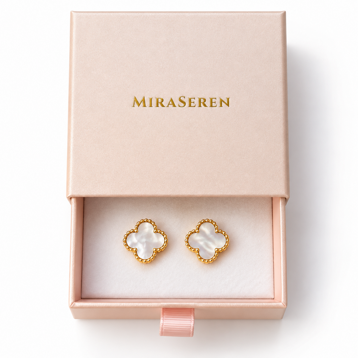A pair of Miraseren four-leaf clover stud earrings with white mother-of-pearl inlays and gold beaded borders, presented in an open blush pink jewelry box with the brand name 'MIRASEREN' in gold on the lid.