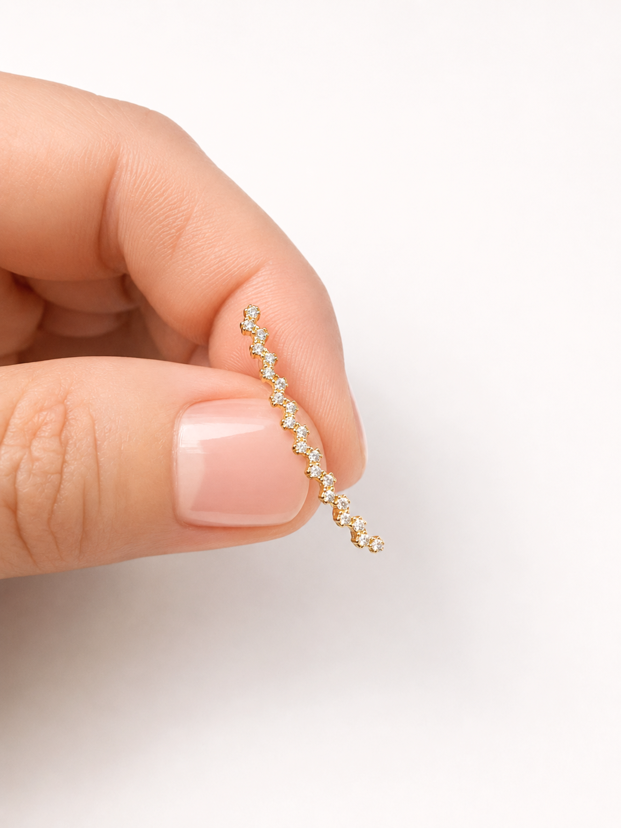 A close-up of a hand holding a delicate gold wire-wrapped diamond necklace against a clean white background.
