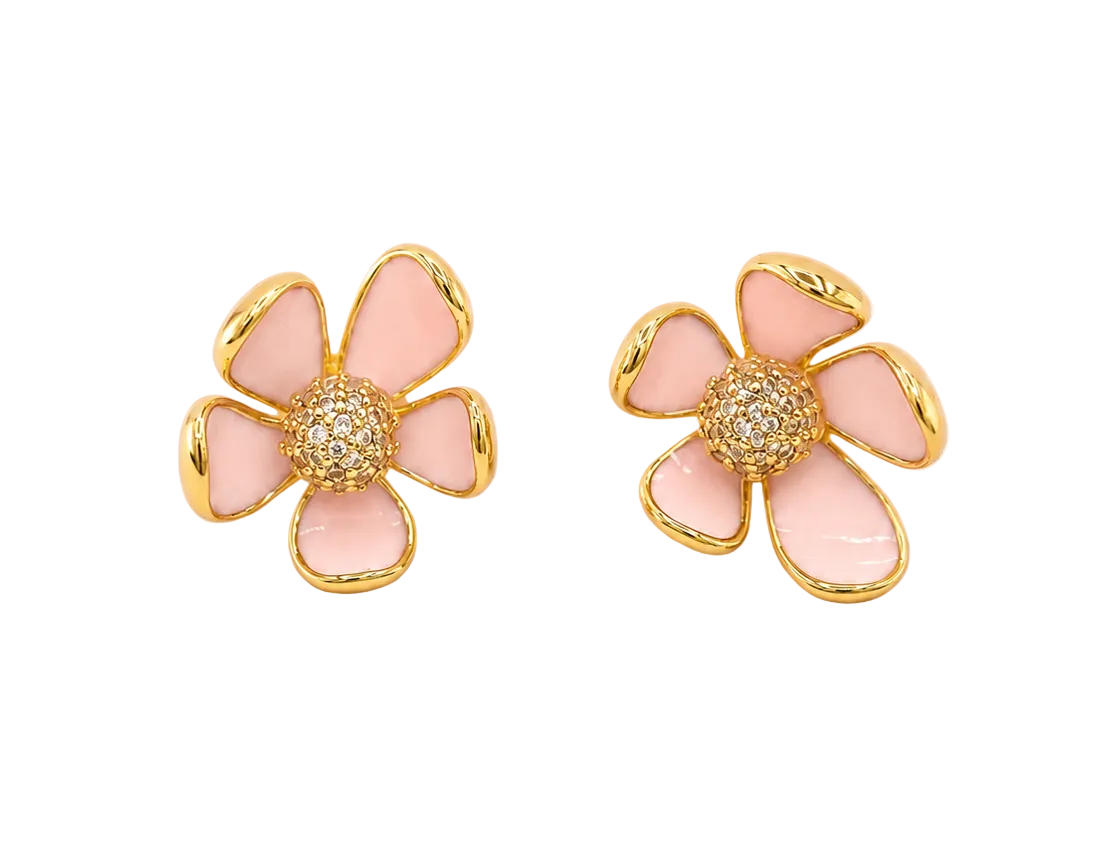 A pair of gold flower-shaped stud earrings with light pink enamel petals and a central cluster of small clear stones, shown on a pale pink background.
