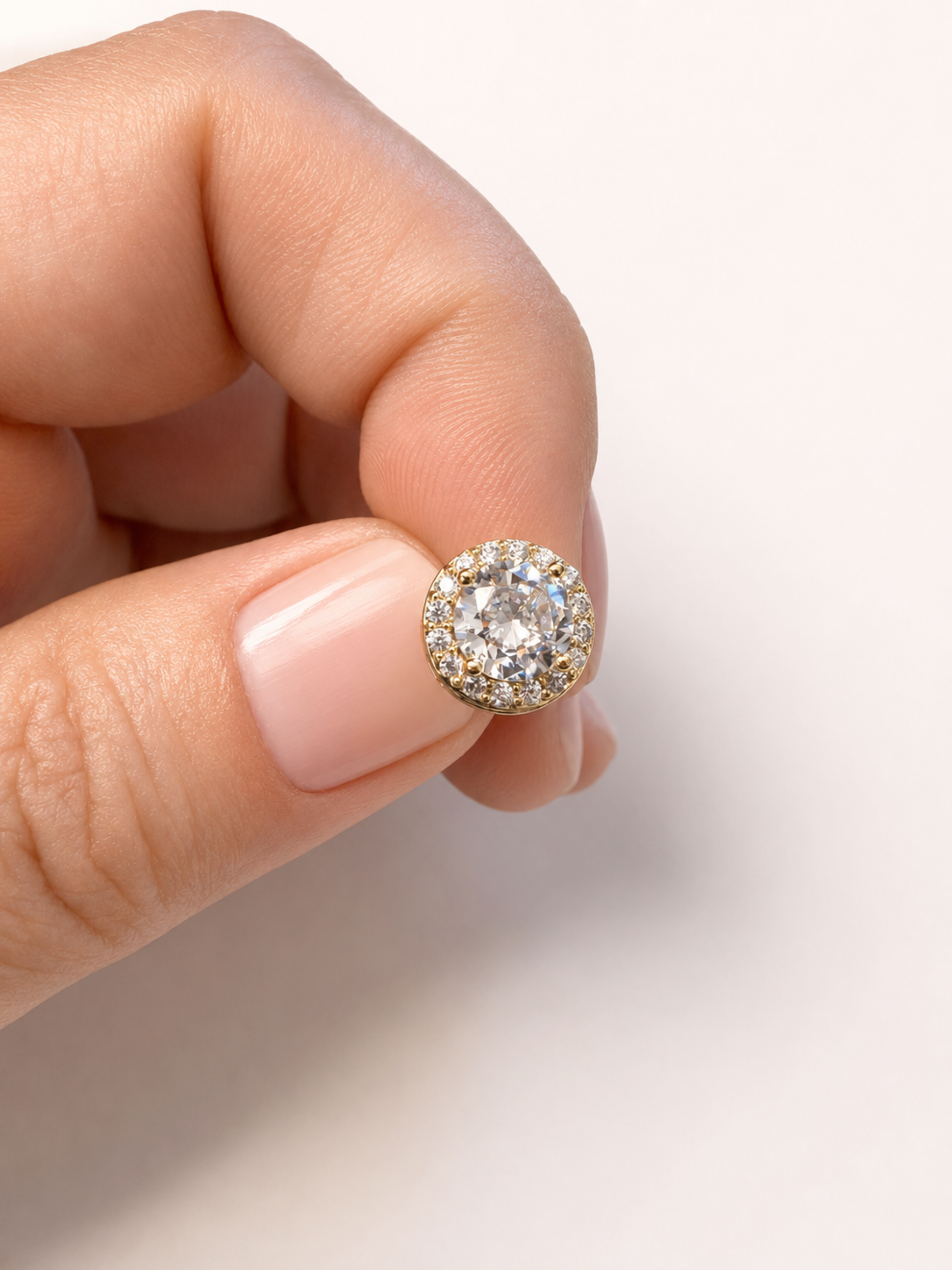 A close-up of a hand holding a round halo diamond ring with a yellow gold setting against a clean white background.
