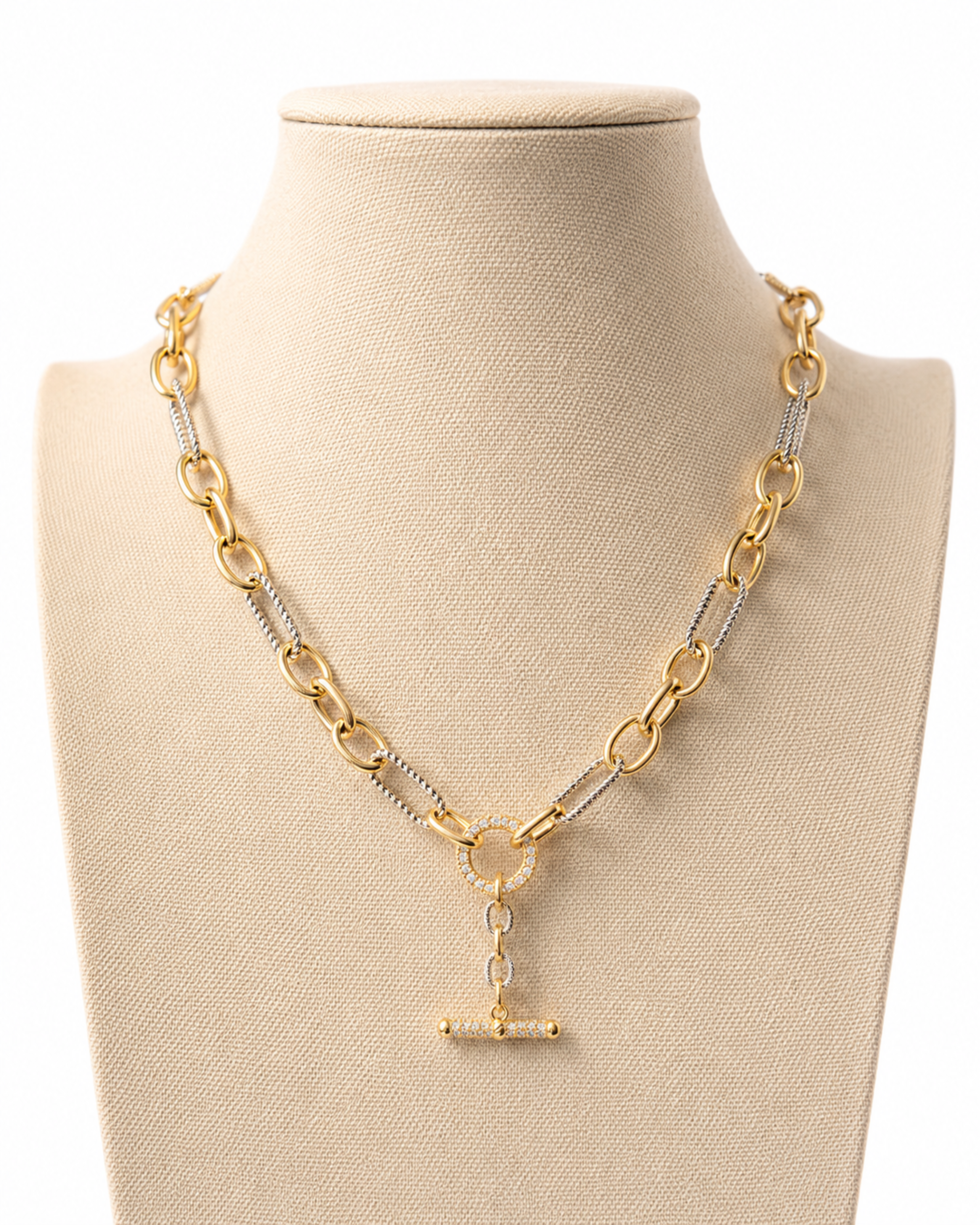 A gold and silver chain necklace displayed on a beige fabric jewelry bust against a white background. The necklace features a gold paperclip chain, silver-toned links with small clear stones, and a gold T-bar clasp pendant with a clear stone.