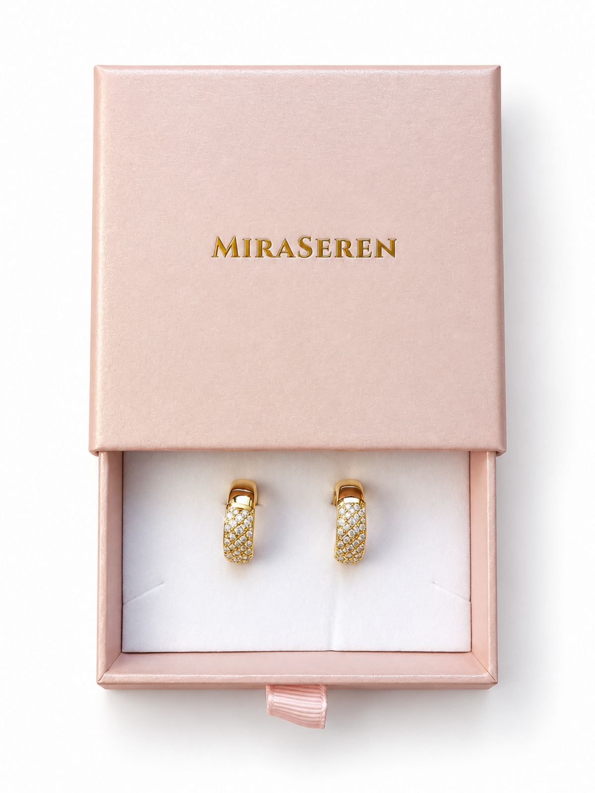 A pair of gold huggie hoop earrings covered in small clear pavé stones, presented in an open pink Miraseren jewelry box on a white background.