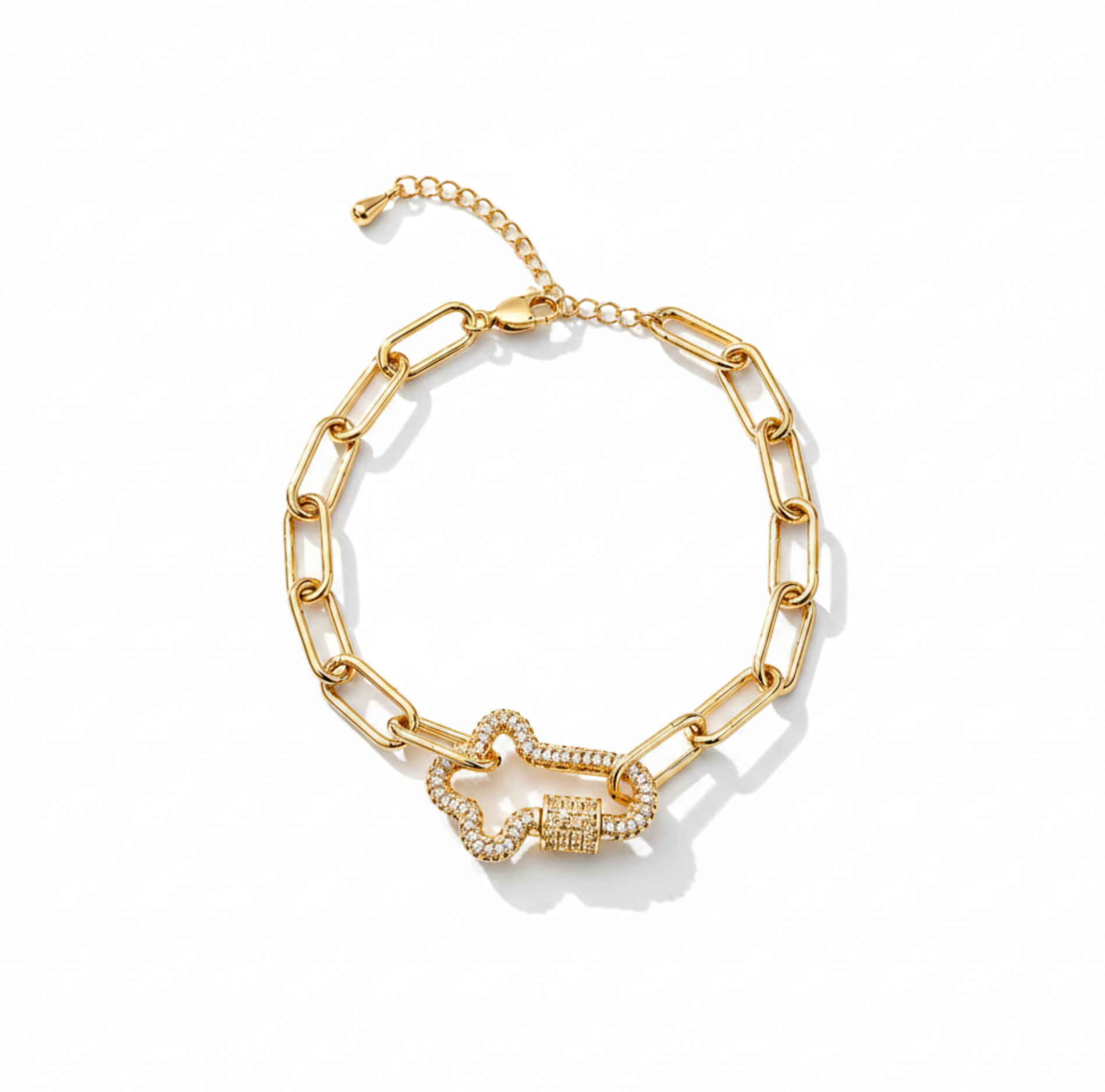A gold-toned chain link bracelet with a central knot-like charm paved with small clear stones, displayed on a light cream background.