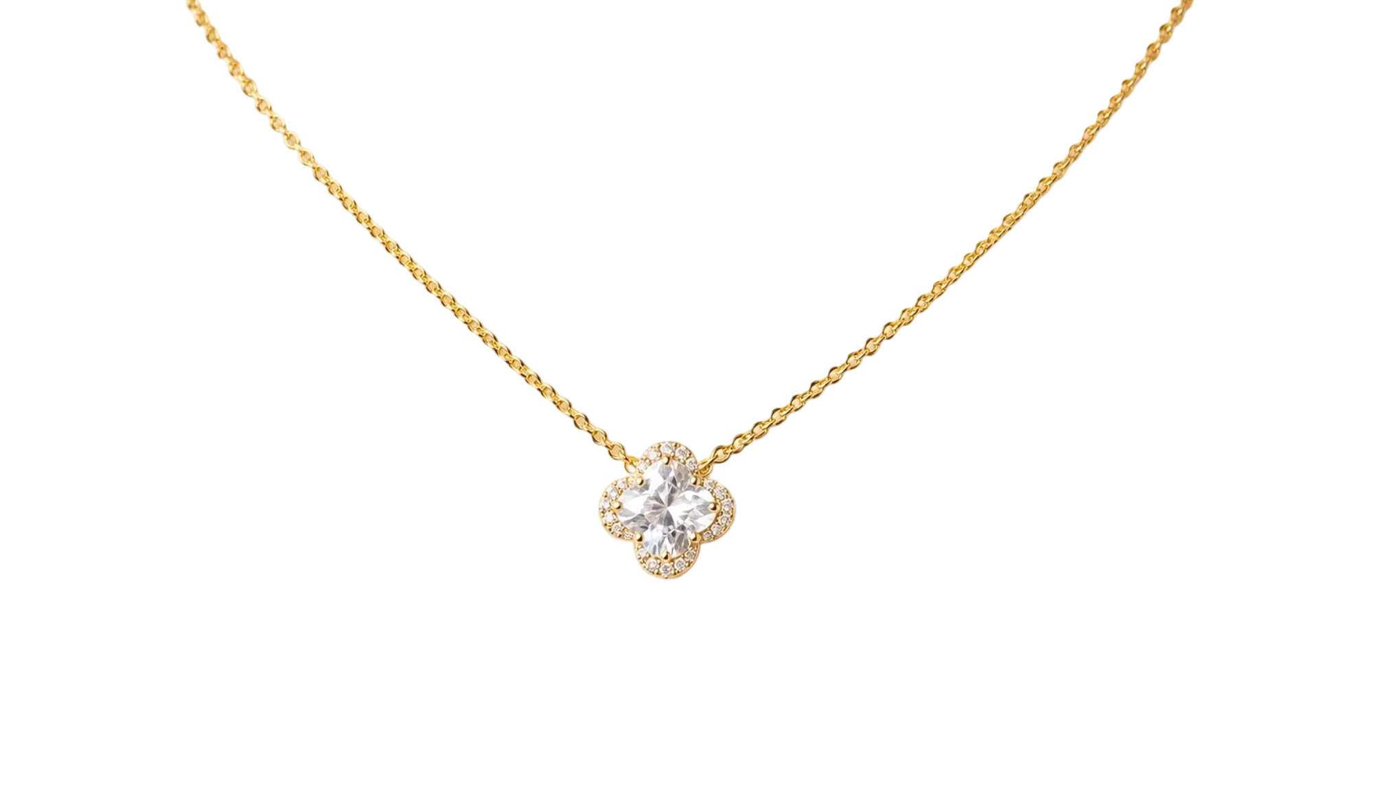 A delicate gold chain necklace with a four-petal flower pendant, featuring a central clear gemstone surrounded by a halo of small clear stones, displayed on a textured beige surface.