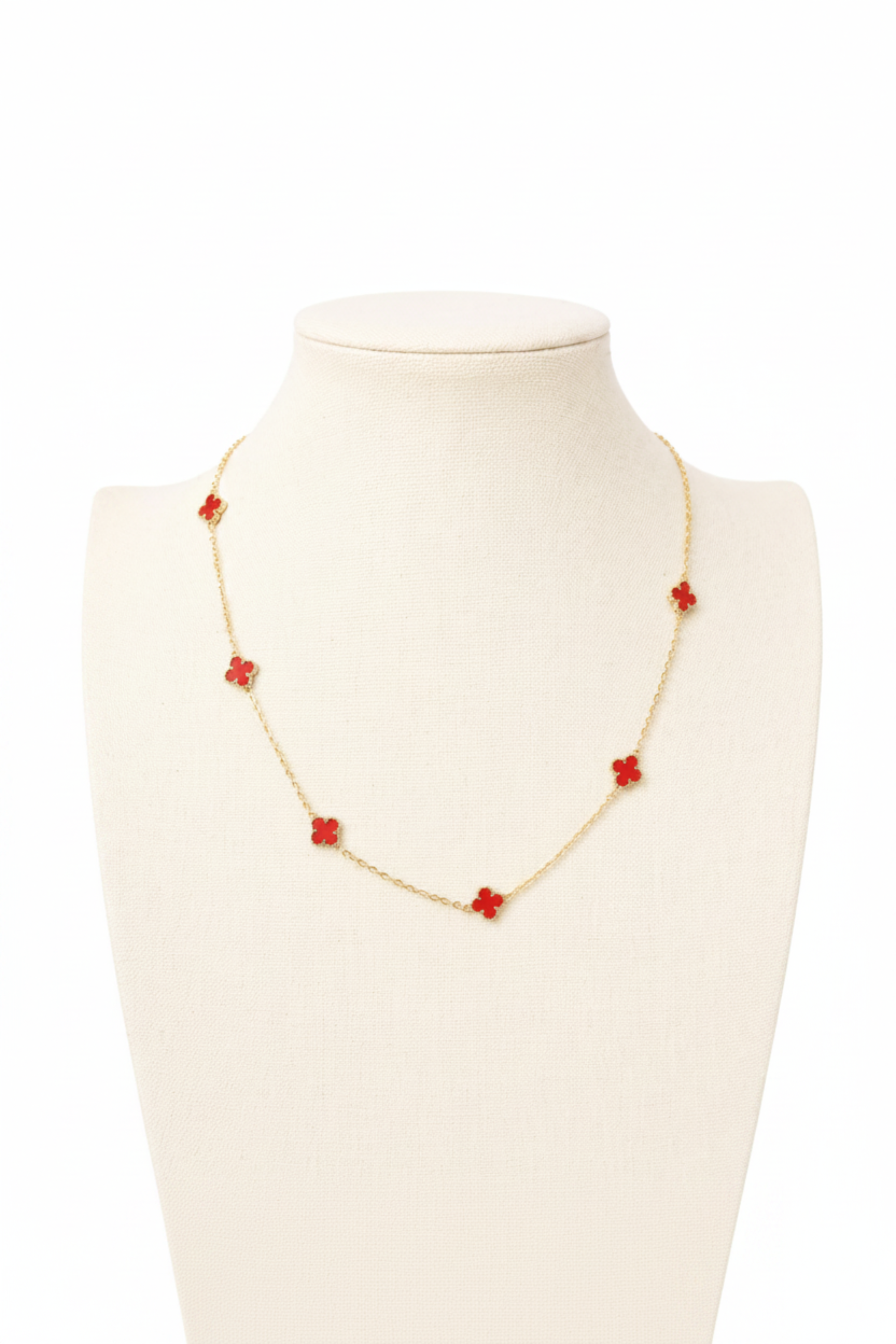 A delicate gold chain necklace with five small red flower-shaped charms, displayed on a cream-colored jewelry bust against a white background.