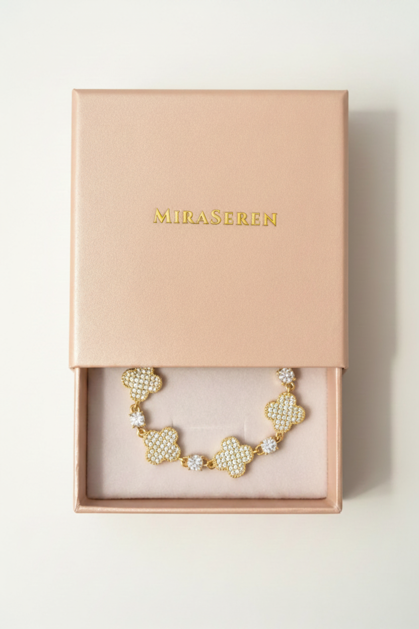 A gold-tone Miraseren bracelet with pavé-set clear stones in a floral starburst design, presented inside an open blush pink Miraseren gift box on a softly lit beige surface.