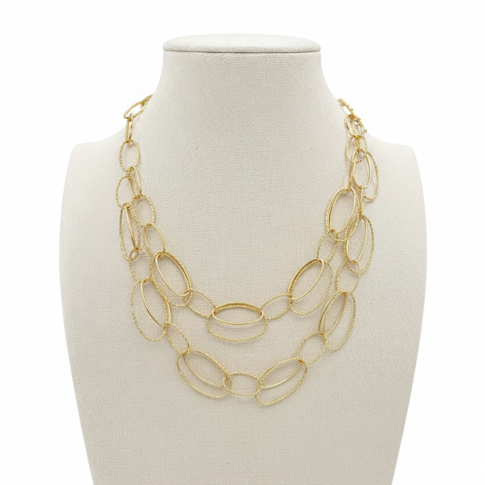 A gold-toned multi-strand statement necklace with textured and smooth oval links, displayed on a cream fabric jewelry bust against a light gray background.