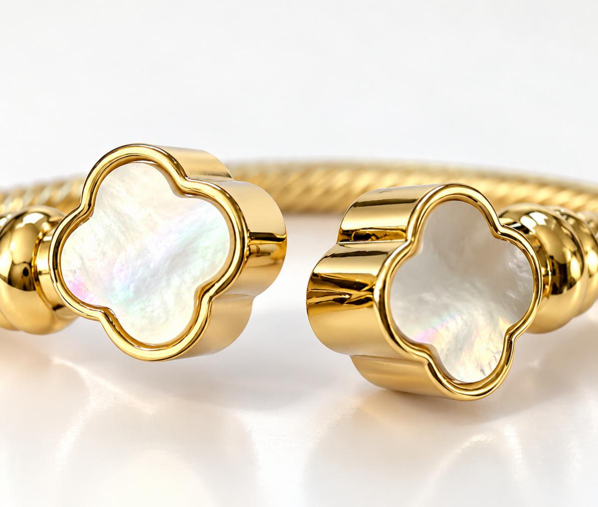 Gold-tone cuff bracelet with four-leaf clover-shaped mother-of-pearl inlays on a clean white background.