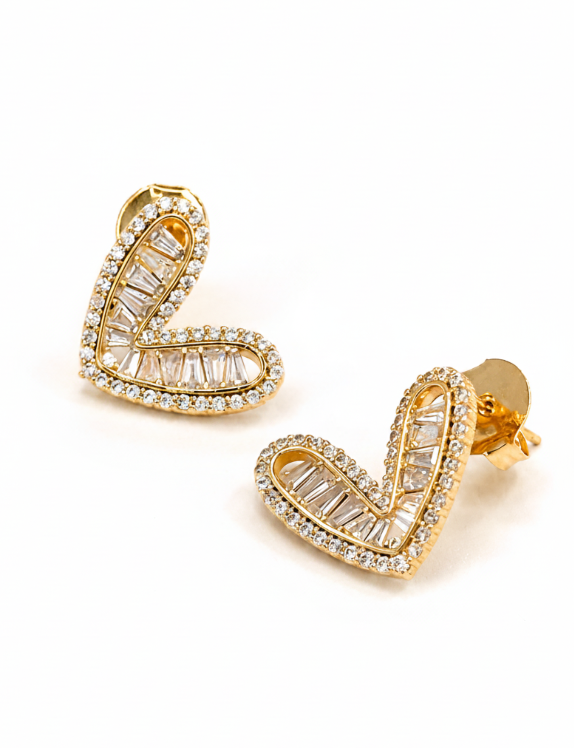 A pair of gold heart-shaped stud earrings adorned with clear baguette and round crystals, shown on a clean white background.