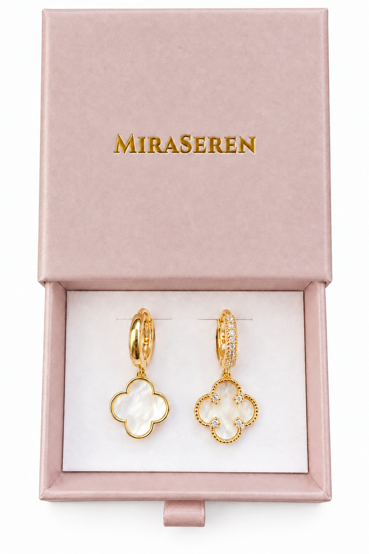 A pair of gold-tone Miraseren drop earrings with mother-of-pearl clover motifs, presented in a pink Miraseren gift box on a wooden surface.