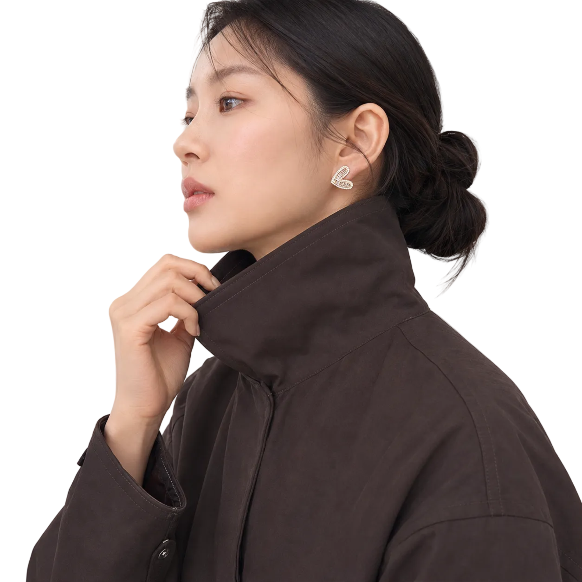 A woman in a dark brown high-collar jacket wearing a small silver bunny-shaped stud earring, shown in a close-up side profile against a light neutral background.