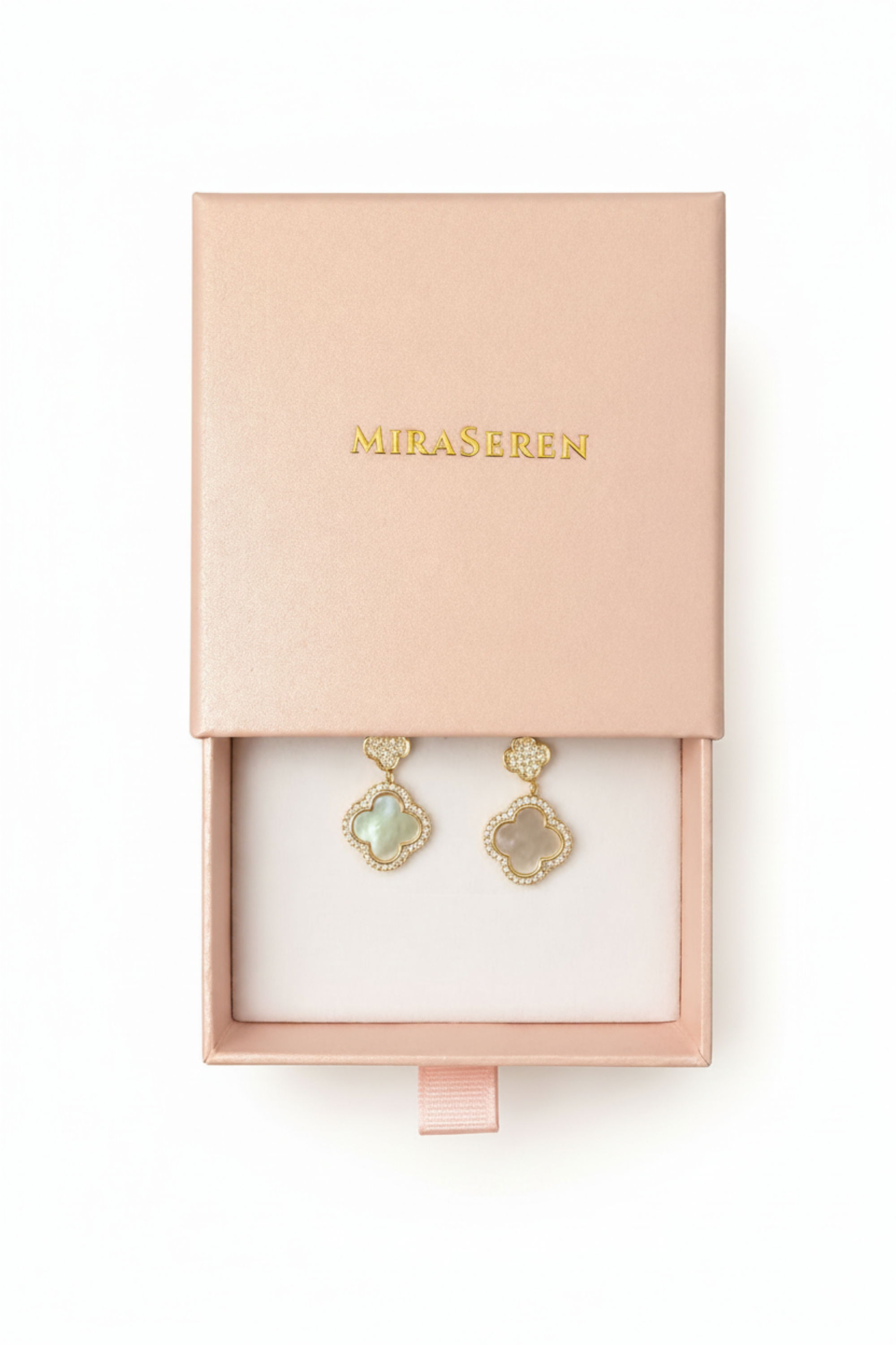 A pair of Miraseren gold-tone drop earrings with iridescent blue-green clover-shaped stones, presented in an open blush pink jewelry box with the brand name gold-embossed on the lid.
