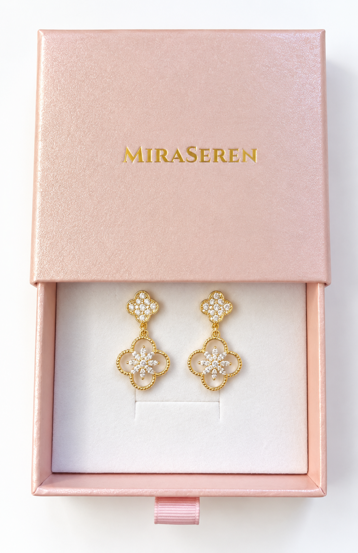 A pair of gold drop earrings with clear crystal-like floral details, presented in a pink Miraseren jewelry box on a white background.
