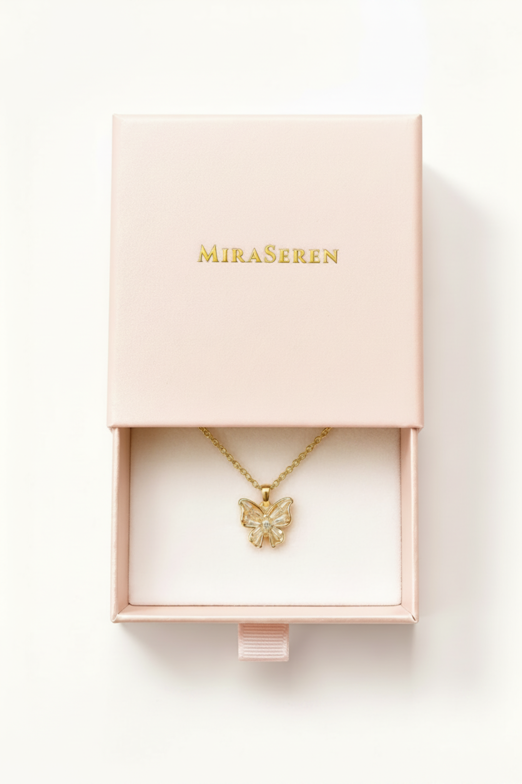 A gold butterfly pendant necklace on a delicate chain, presented inside an open light pink Miraseren jewelry box with gold lettering on the lid, shot against a clean white background.