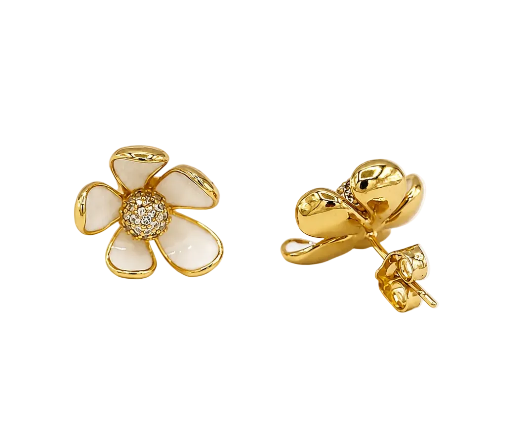 A pair of gold flower stud earrings with white enamel petals and a small clear crystal center, shown on a clean off-white background.