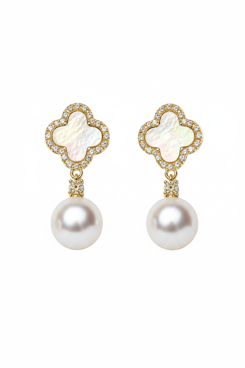 A pair of gold-plated drop earrings featuring a four-leaf clover motif with iridescent mother-of-pearl centers, surrounded by small clear crystals, with a larger white pearl dangling below, set against a clean white background.