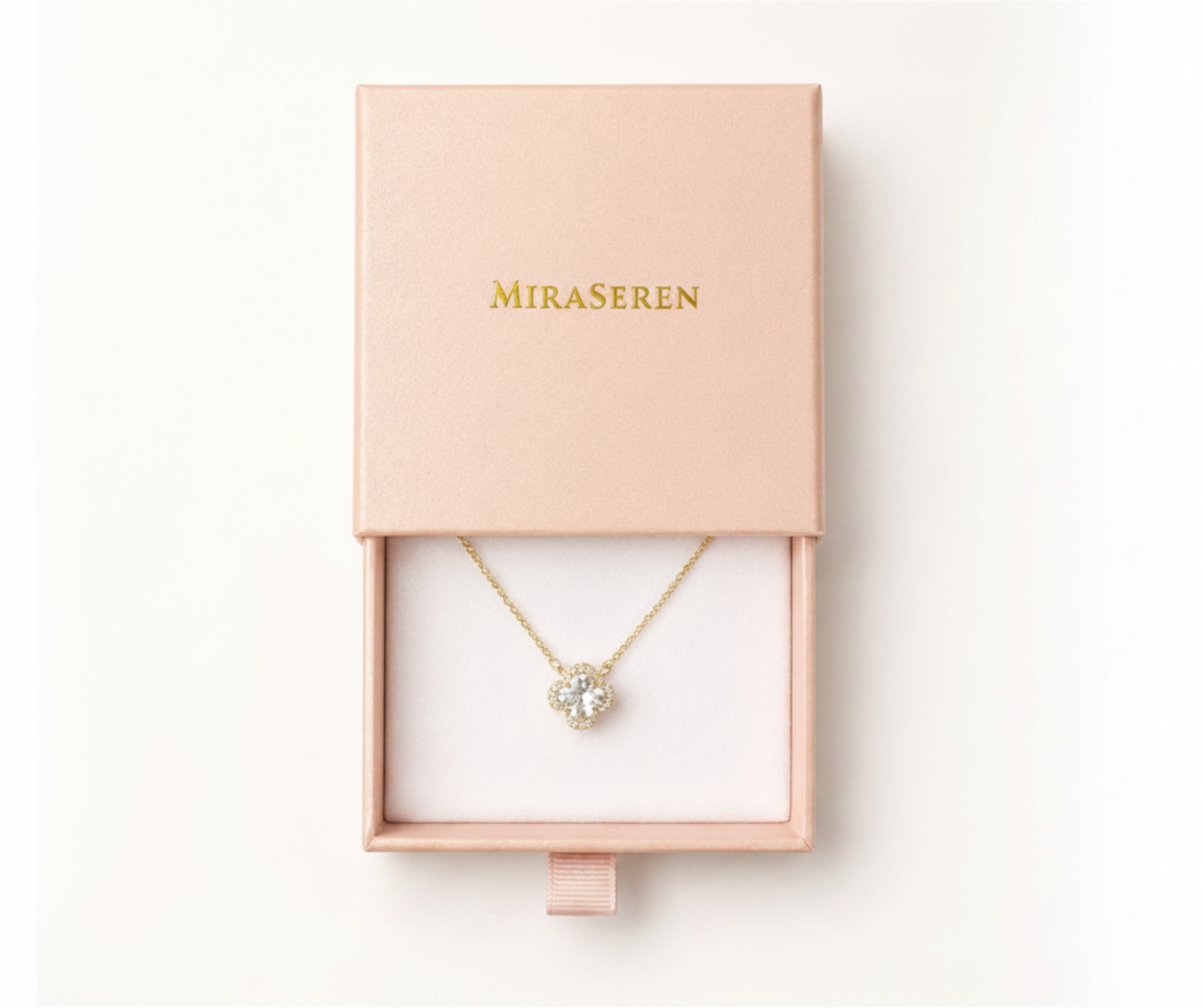 A gold necklace with a clear crystal clover pendant displayed inside an open pink Miraseren jewelry box on a white background.