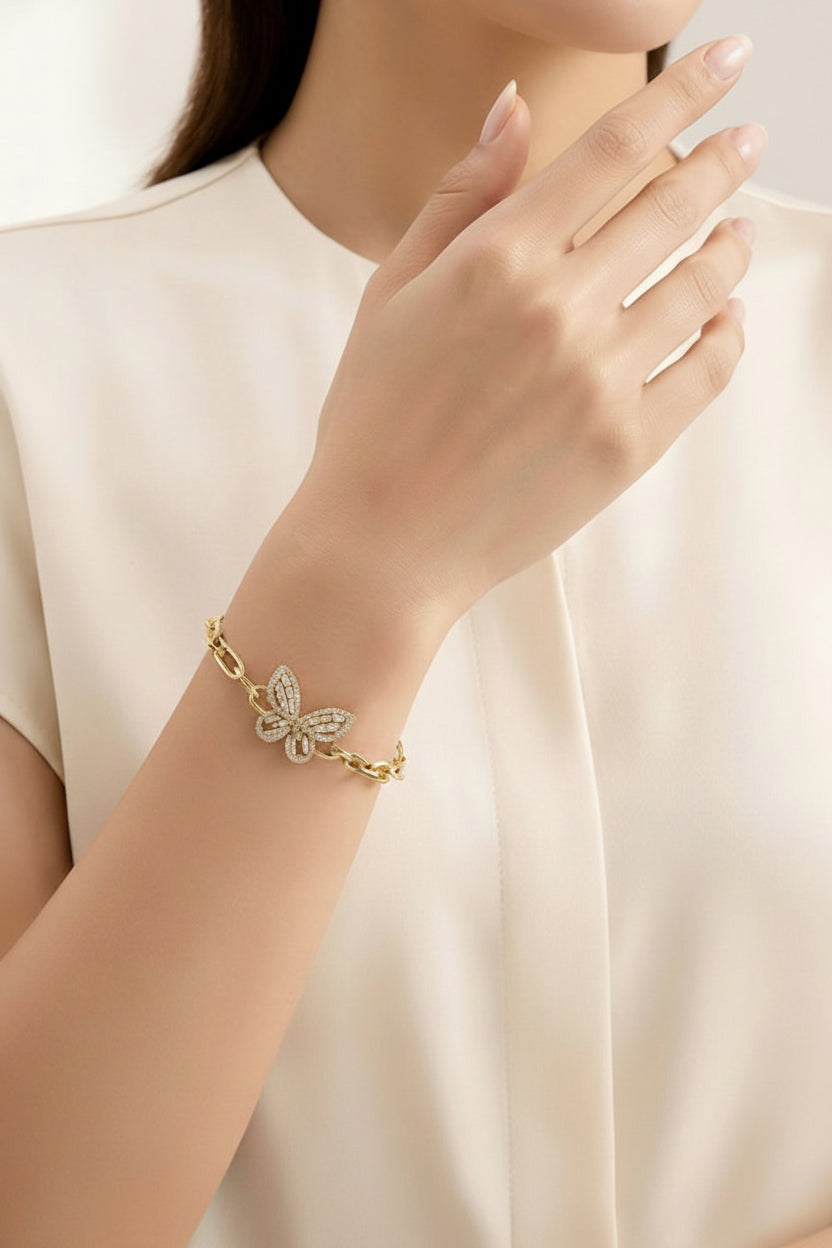 A close-up of a woman wearing a delicate gold butterfly bracelet with sparkling clear stones, paired with a cream-colored blouse.