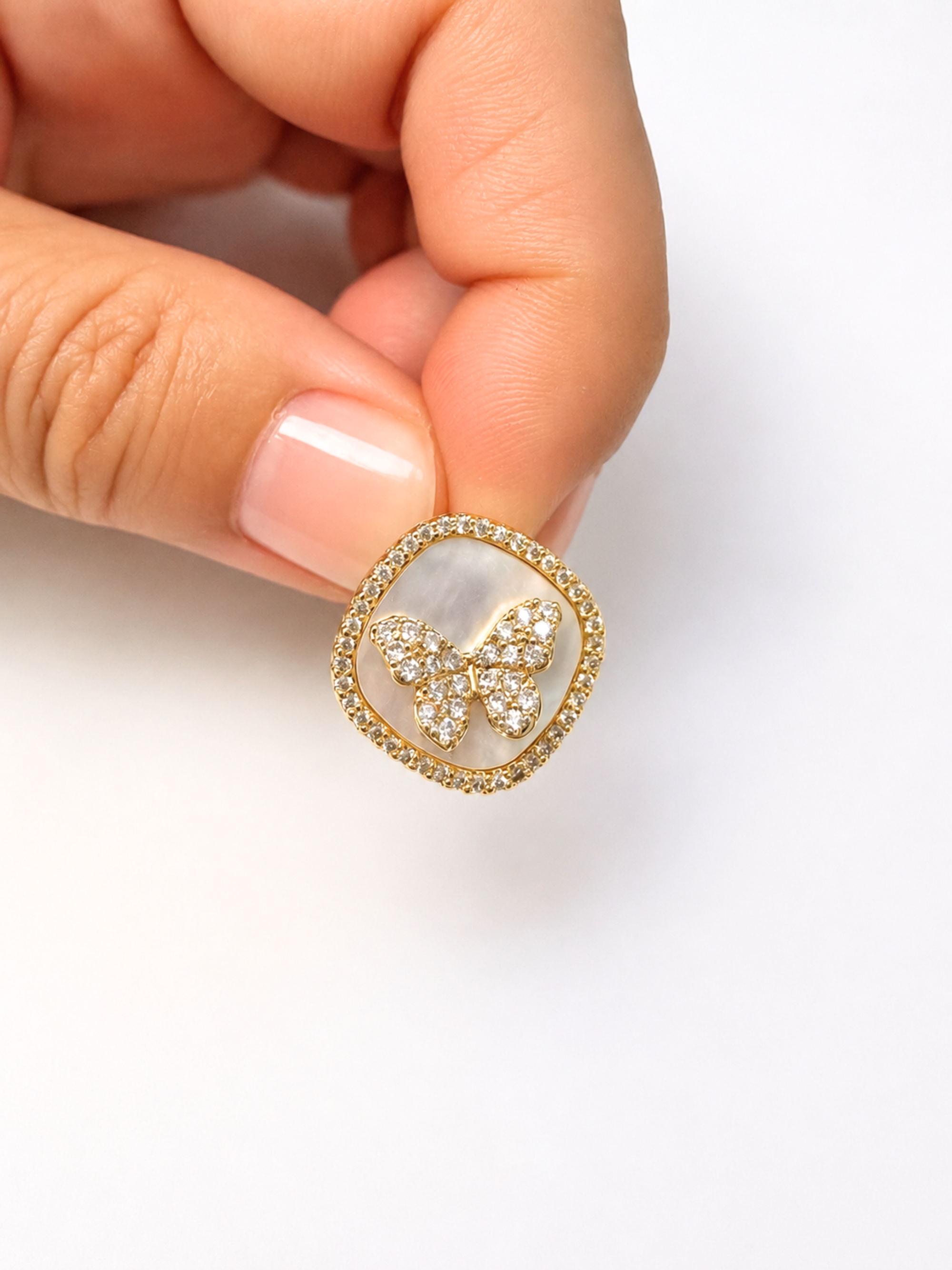 A close-up of a hand holding a gold butterfly ring with a white mother-of-pearl center and small clear stones.