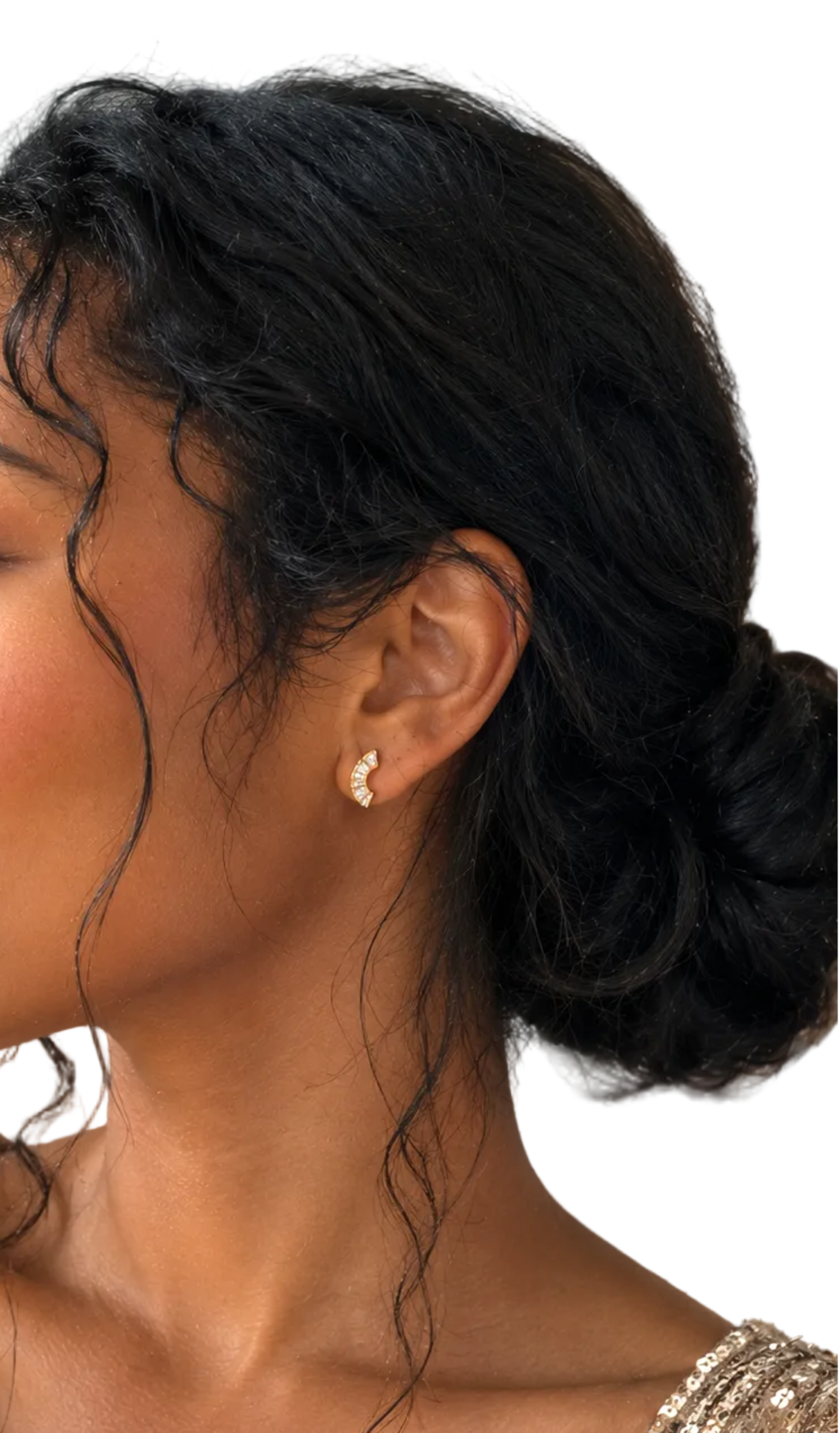 A woman in profile wearing a small gold stud earring, with dark curly hair styled in an updo and a sparkling gold sequined top.