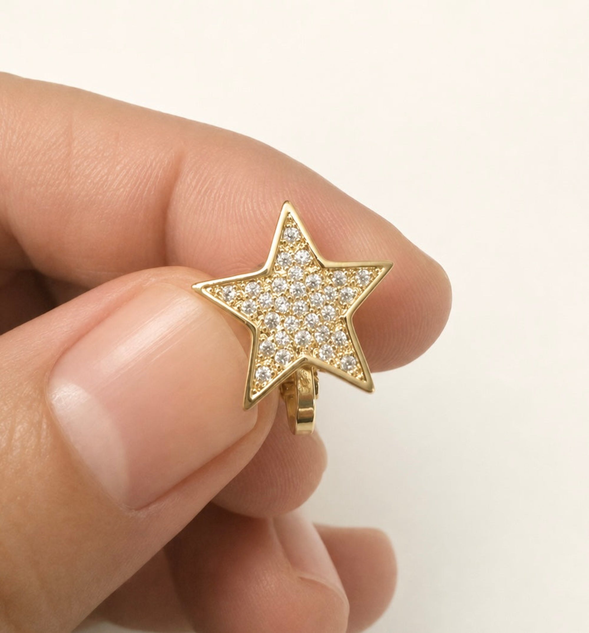 A gold star-shaped ring paved with small clear stones, held between two fingers against a plain white background.