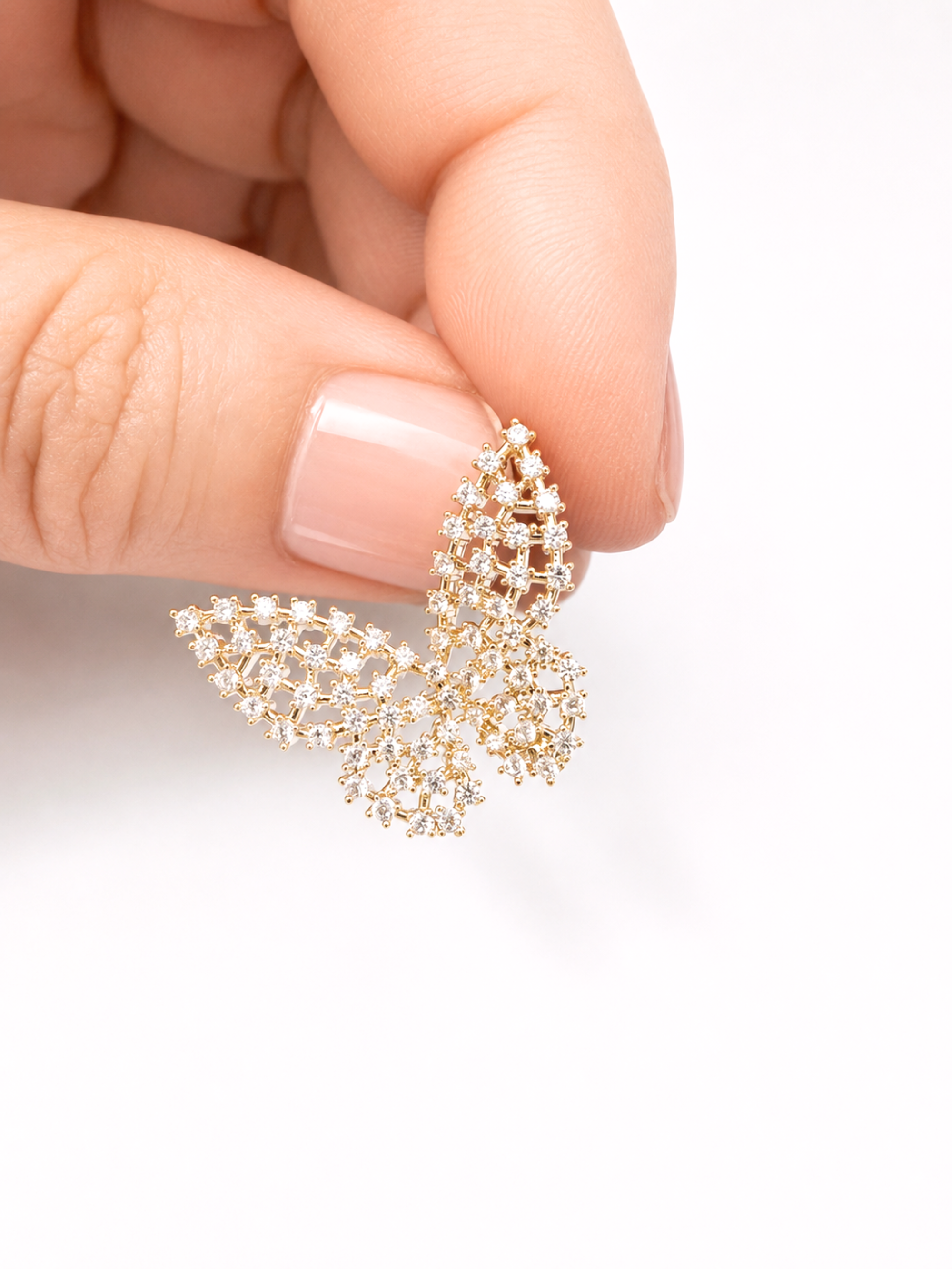 A close-up of a hand holding a gold butterfly-shaped stud earring adorned with small clear crystals, set against a plain white background.