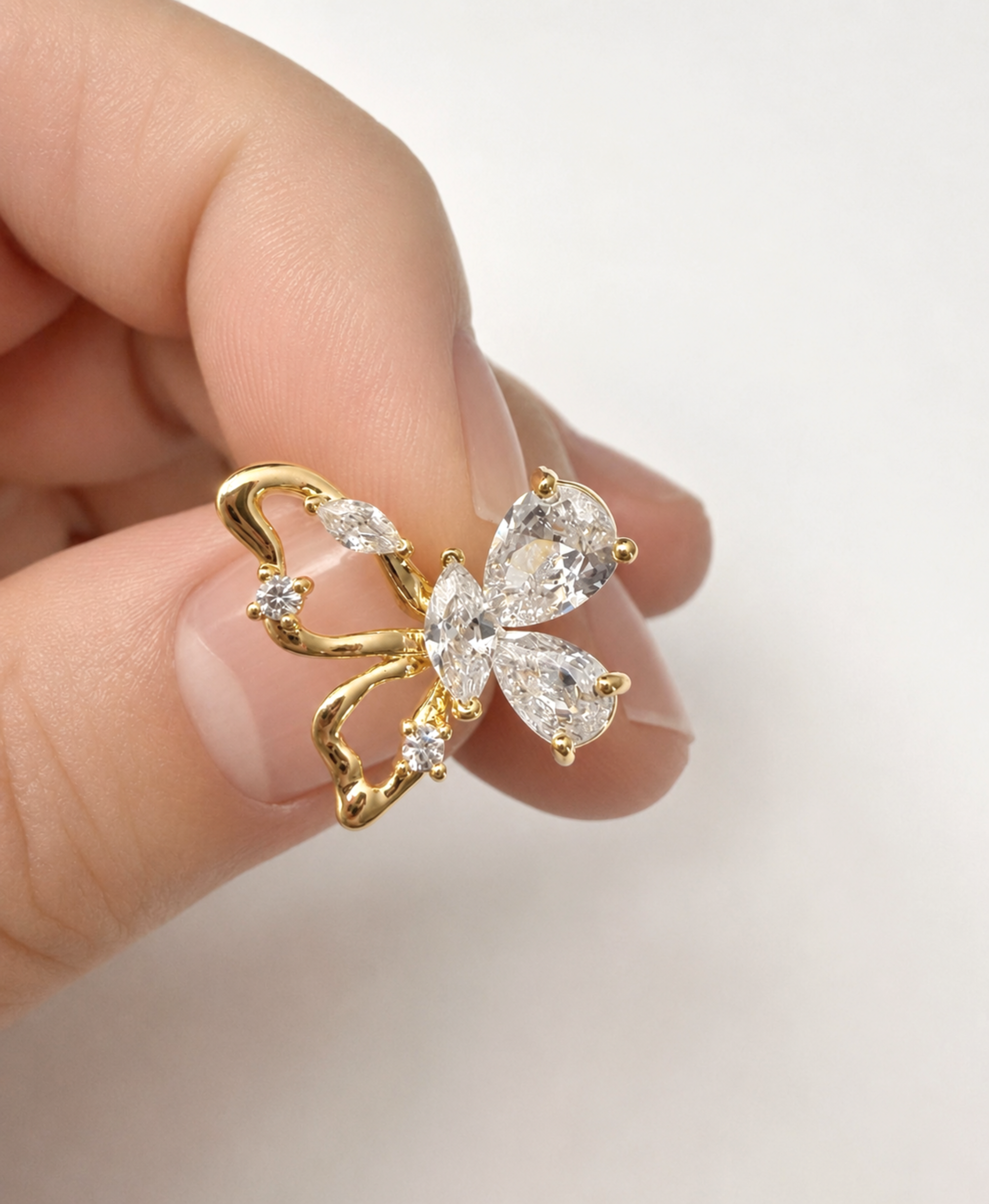 A gold butterfly-shaped ring with clear marquise and round-cut gemstones, shown being worn on a person's finger against a soft white background.